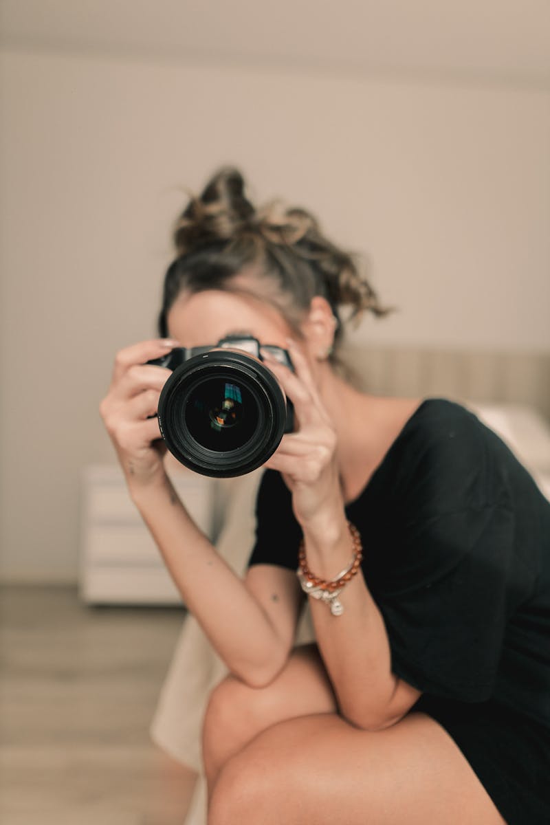 Focused woman taking a photo with a DSLR camera indoors, expressing creativity.